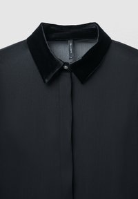 Camicia nera in chiffon con colletto in velluto, dotata di chiusura frontale con bottoni e una sottile texture plissettata su tutto il tessuto.