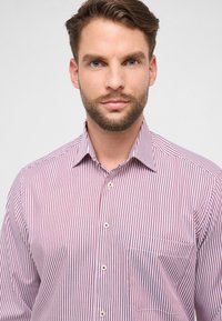 Gestreept overhemd met verticale rood-witte strepen, knoopsluiting aan de voorkant, puntige kraag en een enkele zak aan de linkerkant.