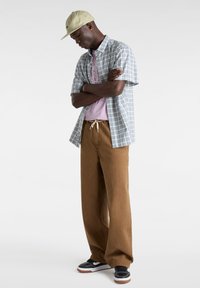 Camisa de cuadros de manga corta en azul y blanco, camiseta gráfica en un tono púrpura claro, pantalones de pierna ancha marrones y zapatillas negras con detalles blancos.