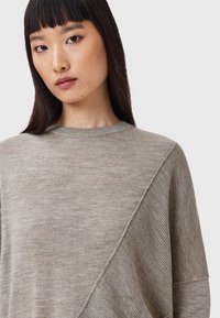 Pullover grigio chiaro con scollatura a girocollo, caratterizzato da una texture a coste diagonali e dettagli a maglia liscia. Tessuto morbido e leggero.