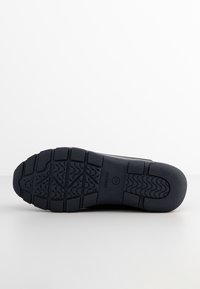 Suela de zapato de goma negra con un patrón de agarre texturizado, que presenta ranuras y acentos circulares para tracción y flexibilidad.