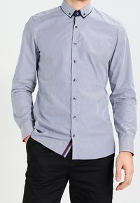 Proužkovaná košile v modré a bílé barvě s límečkem na knoflíky a kontrastními knoflíky. Dlouhé rukávy s detailem manžety.