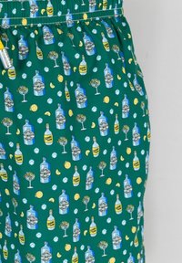 Pantalones cortos de tela verde con un patrón repetido de botellas azules, cócteles, limones y cubos de hielo. Cintura elástica para mayor comodidad.