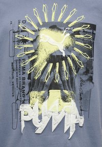 Λογότυπο Puma με κίτρινες ακτίνες ήλιου, αφηρημένο μαύρο και λευκό φόντο, και έντονο υφασματικό κείμενο «PUMA» σε γκρι ύφασμα.