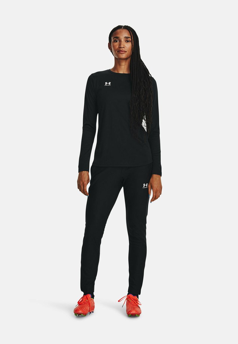 Haut à manches longues noir et pantalon assorti. Le haut présente un logo blanc. Baskets de sport rouges vives avec des accents noir et violet.