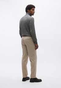 Maglione grigio a collo alto a coste, pantaloni beige, scarpe nere. Design semplice, stile aderente, texture morbida e dettagli minimalisti.