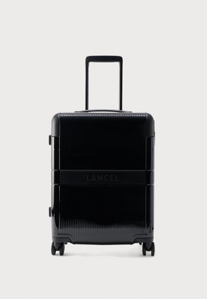 Čierny pevný kufor s teleskopickou rukoväťou, štyrmi otočnými kolieskami a logom "LANCEL" na prednej strane v strede.