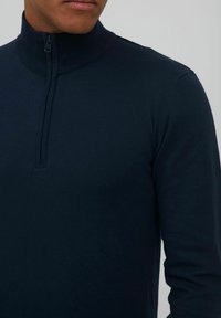 Granatowy sweter z wysokim kołnierzem i zamkiem, o prążkowanej strukturze i dopasowanym kroju, prezentujący gładki materiał i czyste linie.