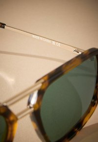 Tortoiseshell sunglasses with green lenses, metallic accents on the temples, labeled "MADE IN CHINA" on one arm.