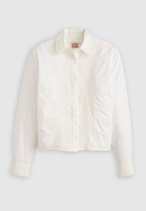 Camisa blanca de botón hecha de algodón con un panel de encaje en el frente y un borde de encaje en el collar y los puños. Diseño recortado.