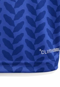 Tela azul con patrones de hojas azul oscuro y texto blanco "Climacool" cerca del borde cosido de una prenda.