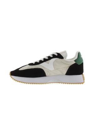 Sneakers with a black and white color scheme, featuring a padded upper, suede accents, a green heel patch, and a textured gum sole.