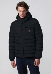 Giacca a vento nera con pannelli cuciti orizzontalmente, zip frontale e tasca sul petto con logo. Il materiale appare liscio e isolato.