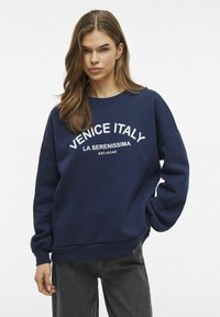 Mornarsko plava dukserica s bijelim tekstom "VENECIJA ITALIJA LA SERENISSIMA EST. 421AD," s okruglim izrezom, dugim rukavima i opuštenim krojem.