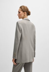 Lys grå skræddersyet blazer med en strømlinet silhuet, enkeltstående knaplukning og dekorative knapper på ærmet. Glat stofstruktur.