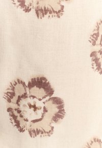 Tkanina s cvetličnim vzorcem v krem barvi z mehkimi, zamegljenimi cvetovi v mauve barvi. Tekstura izgleda rahlo groba in podobna lanu, s naravnim zaključkom.