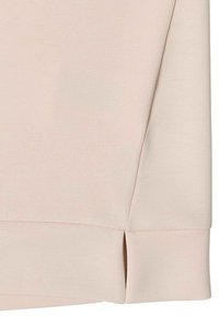 Haut beige clair en tissu lisse, avec un ourlet arrondi et des fentes latérales, au design classique.