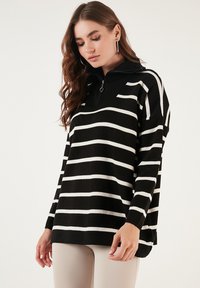Pulover cu dungi alb-negru, cu guler înalt cu fermoar, croială oversized și textură moale, având dungi orizontale pe întreaga suprafață.