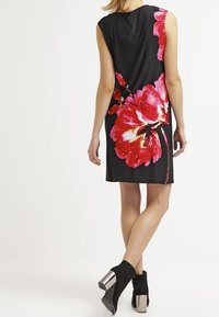 Černé bezruční šaty s velkým růžovým květinovým vzorem; hladká látka se rovnými liniemi; doplněné černými kotníkovými botami s kovovým podpatkem.