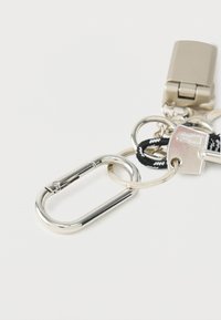 Porte-clés avec des éléments métalliques argentés, comprenant un mousqueton, des anneaux circulaires et un petit cadenas avec un cordon tressé noir et blanc texturé.