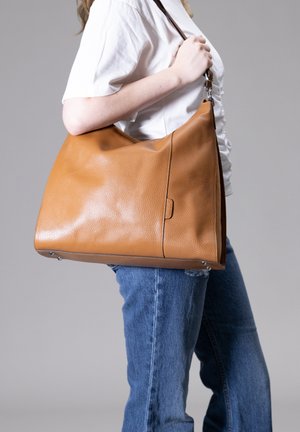Grote karamelkleurige leren handtas met een gepolijste textuur, een ronde vorm en een enkele schouderriem, voorzien van een zijdetail en metalen hardware.