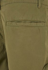 Pantaloni din bumbac verde măsliniu cu o textură netedă, care includ un buzunar cu aplicație și accente cusute pentru durabilitate.