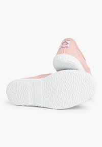 Baskets en toile rose clair avec des semelles en caoutchouc blanc et des motifs texturés ; dotées d'un patch amusant sur le talon indiquant "Fabriqué en Espagne."