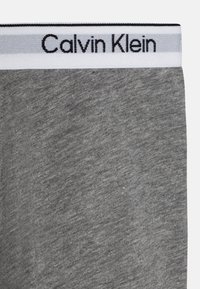 Grå bomullsstoff med en jevn tekstur, med en hvit midjebånd som har en svart "Calvin Klein"-logo.