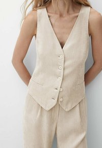 Beige Corduroy-Weste mit tiefem V-Ausschnitt, fünf Knöpfen und zwei frontalen Taschen, kombiniert mit passenden plissierten Hosen. Strukturierter Stoff.