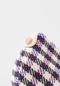 Sac tissé en crème, noir et rose avec un motif géométrique. Présente une forme arrondie et un détail de bouton-pression doré.