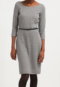 Robe grise à motifs avec manches trois-quarts, encolure ronde et silhouette cintrée. Comprend une fine ceinture noire à la taille.