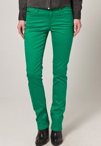 Groene stretchdenim jeans met een slim fit, voorzien van voorzakken en een ritssluiting, gecombineerd met zwarte enkellaarsjes.