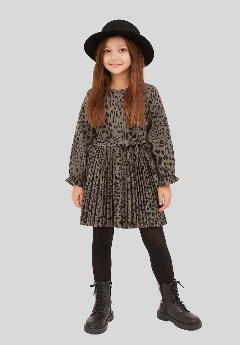 Mädchenkleid in Dunkelgrün mit Leopardenmuster, plissiertem Rock, langen Ärmeln und einem Gürtel, kombiniert mit schwarzen Leggings und Kampfstiefeln.