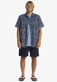 Short-sleeve button-up shirt with a dark floral pattern, paired with a light blue t-shirt, navy shorts, and black sandals.