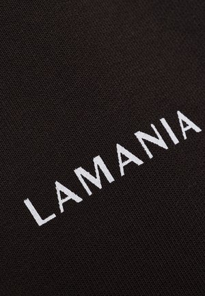 Textul alb brodat "LAMANIA" pe un fundal de stofă texturată neagră, prezentat dintr-un unghi.