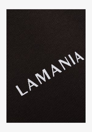 Textul alb brodat "LAMANIA" pe un fundal de stofă texturată neagră, prezentat dintr-un unghi.