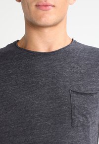 Dunkelgraues T-Shirt mit kurzen Ärmeln aus weichem Stoff, mit runder Ausschnitt und einer kleinen Tasche auf der linken Seite.