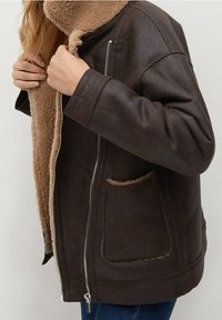Brązowa skórzana kurtka z miękkim, tanowym futerkiem w środku, z zamkiem błyskawicznym i kieszeniami po bokach. Posiada luźny krój i szeroki design kołnierza.