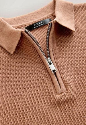 Světle hnědý bavlněný svetr s límcem na zip, s texturovaným povrchem a stříbrnými detaily. Nálepka viditelná na výstřihu.