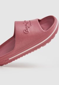 Sandale à glissière en caoutchouc rose avec une large bride, une semelle intérieure texturée et des lignes d'accent blanches sur la semelle. Logo embossé sur la bride.