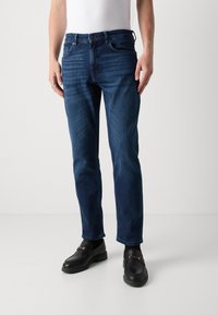 Jeans in denim blu scuro con vestibilità dritta, design a cinque tasche, dettagli cuciti e chiusura con bottone. Presenta una leggera scoloritura sulle cosce.
