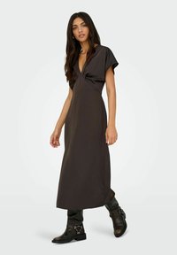 Juodas maxi suknelė su gilia V formos iškirpte, trumpomis rankovėmis ir drapiruotu audiniu. Dėvima kartu su juodomis aulinėmis batais iki kelių, su sagtimis.