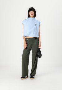 Top corto azzurro con maniche a sbuffo, abbinato a pantaloni larghi verde oliva. Una borsa nera e calzature completano l'outfit.