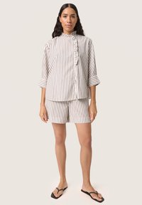 Stribet top og shorts sæt i blødt stof, med en flæseknapstolpe og trekvartærmer. Farverne er beige og grå striber.