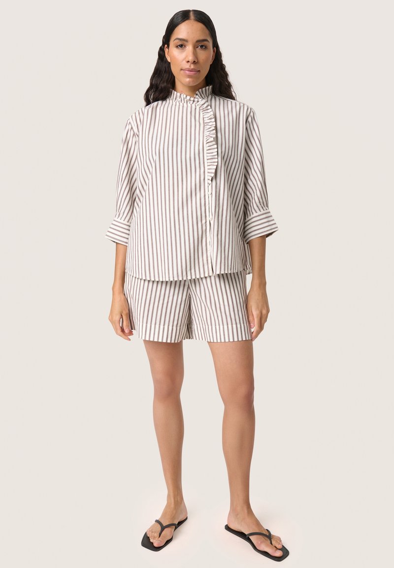 Stribet top og shorts sæt i blødt stof, med en flæseknapstolpe og trekvartærmer. Farverne er beige og grå striber.