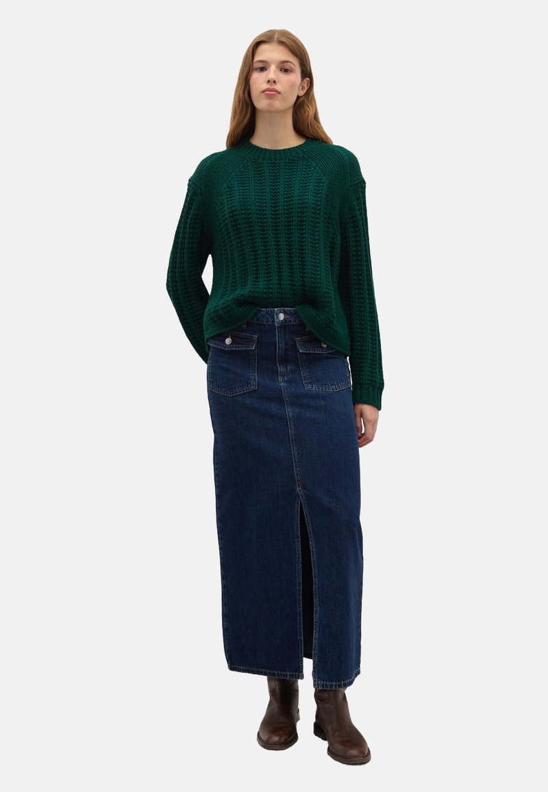 Groene gebreide trui met een losse pasvorm en ribbeltextuur, gecombineerd met een donkerdenim maxi rok met een split aan de voorkant en achterzakken.