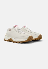 White leather sneakers feature a textured tan rubber sole, round laces, and a red logo tab at the tongue, designed for comfort and durability.