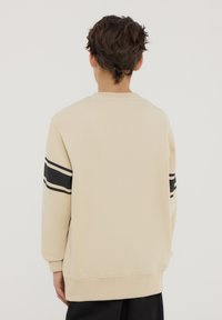 Felpa beige con strisce orizzontali bianche e nere sulle maniche. Caratterizzata da un collo tondo e polsini a coste. Texture liscia.