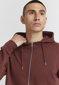 Bordeaux zip-up hettegenser med snor i hetta, myk tekstur og metallglidelås. Har en tettsittende design og ribbede mansjetter for en komfortabel passform.