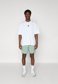 T-shirt blanche oversized avec logo noir ; shorts verts ; baskets blanches ; design simple, manches courtes, coupe décontractée, tissu texturé.